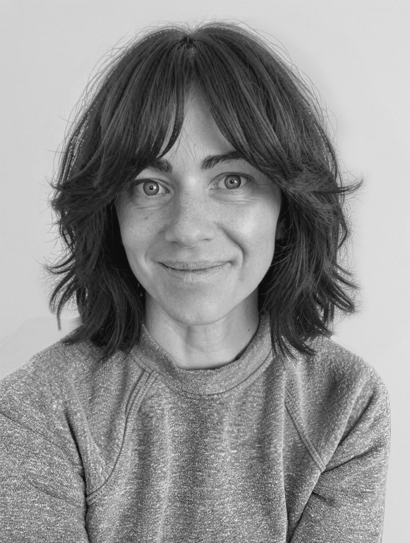 Black and white headshot of a woman with dark, layered hair and a grey sweatshirt.