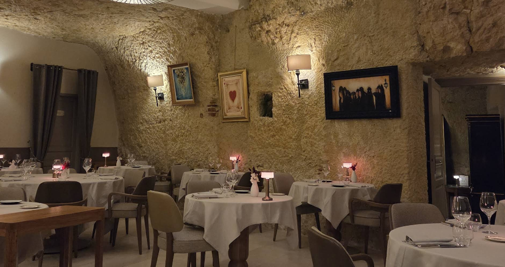 Une salle de restaurant tamisée, murs de pierre, tableaux encadrés et tables dressées avec soin.