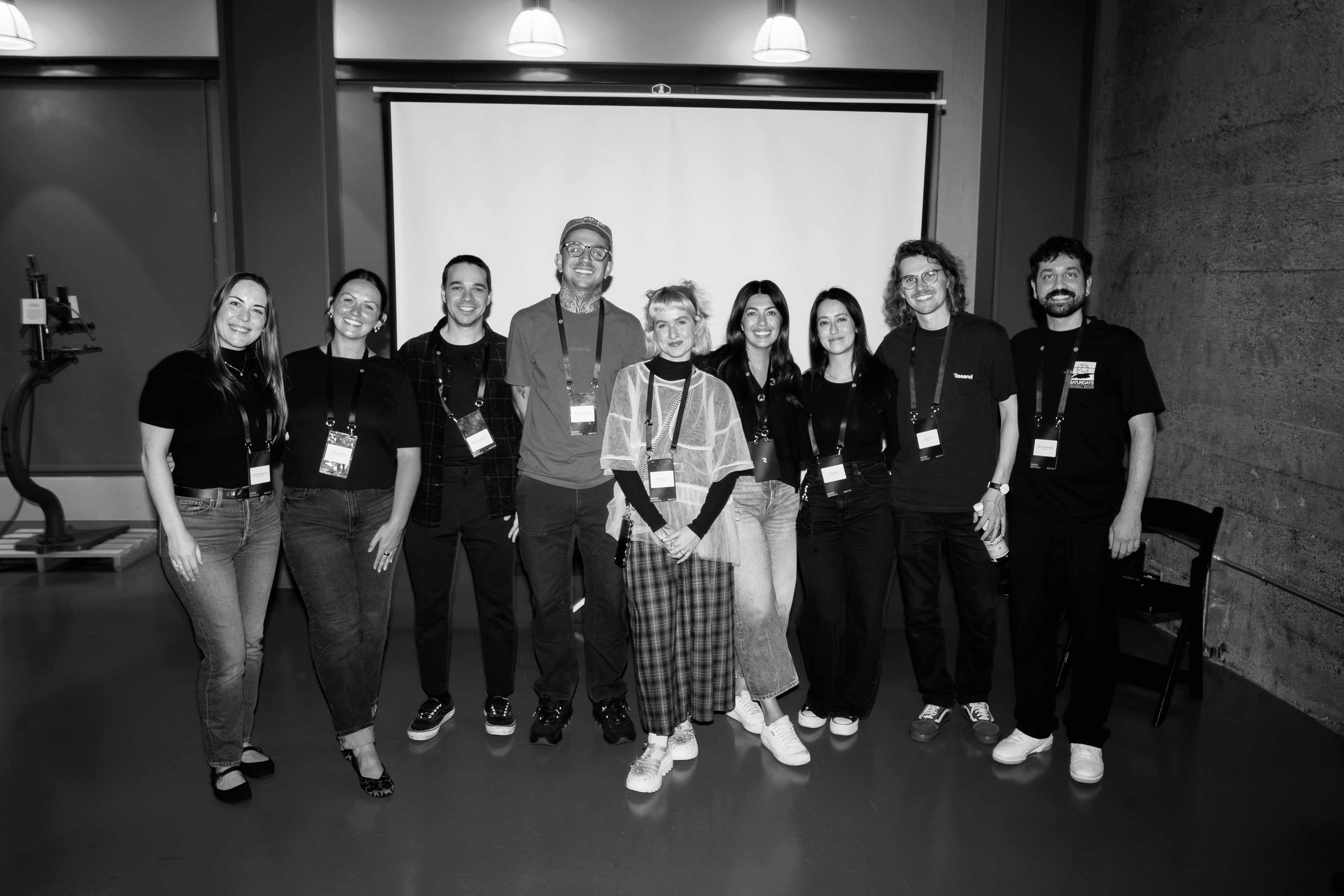 A group of nine people, five women and four men, pose for a photo in front of a projector screen.