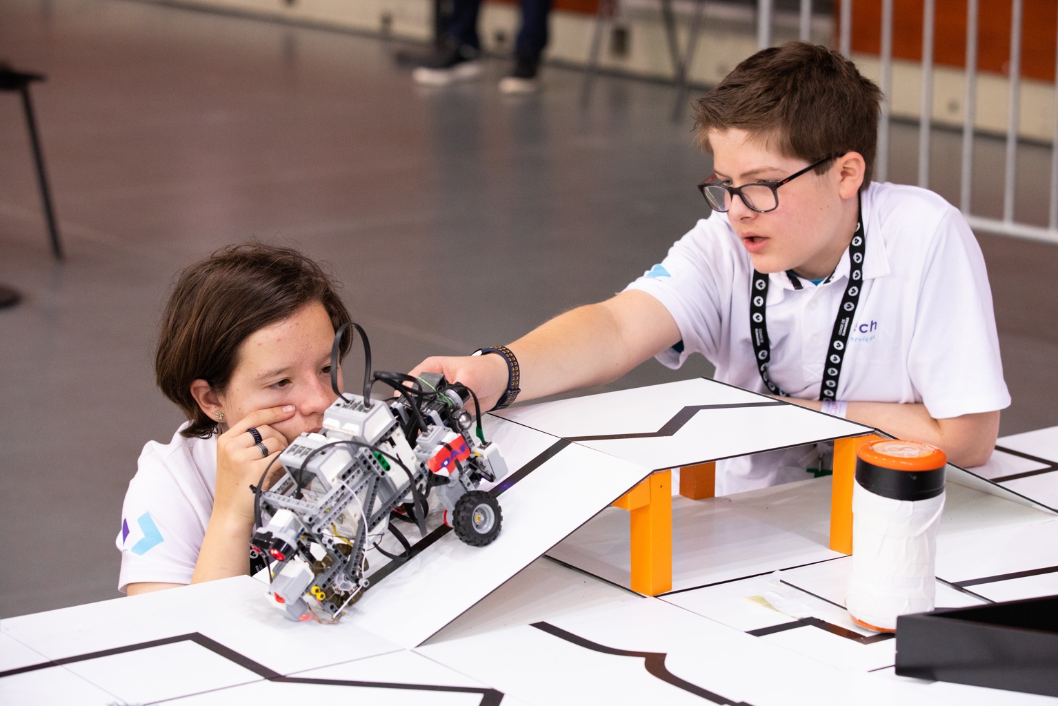 Two young students focus intently on a complex Lego robot on a white competition course.