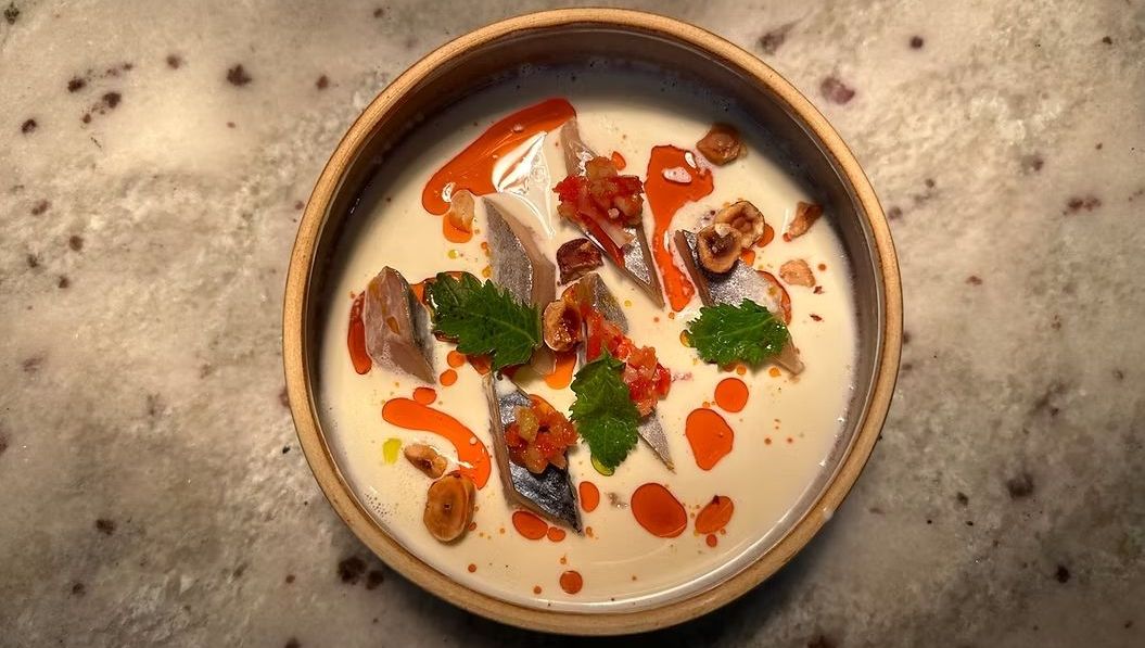 Une soupe crémeuse avec des morceaux de poisson, une sauce rouge, des herbes et des noix.