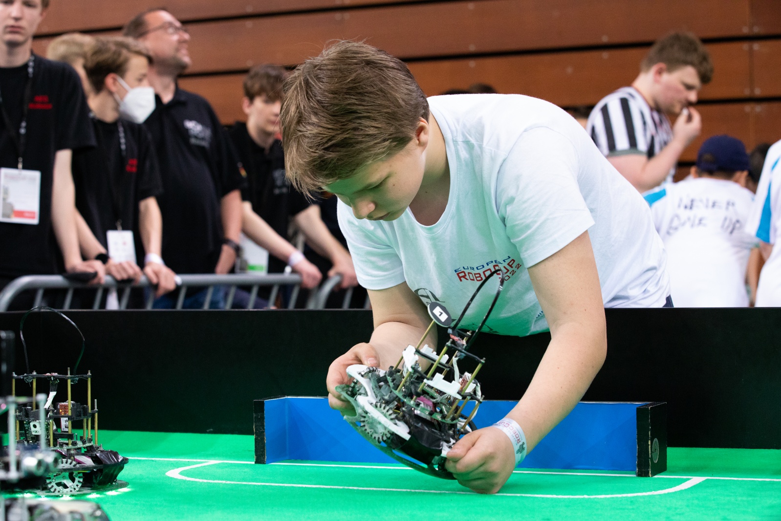 Um jovem participante em uma competição de robótica ajusta um robô em um campo verde.