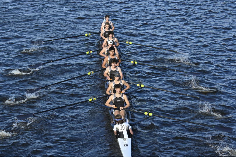 A team of eight rowers in a racing shell moves in unison on the water.