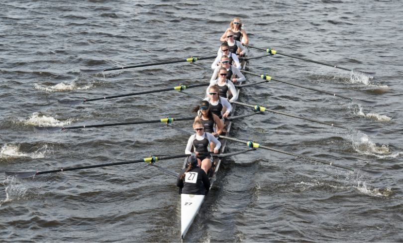 A team of eight women in a rowing shell propels themselves through the water with synchronized strokes.