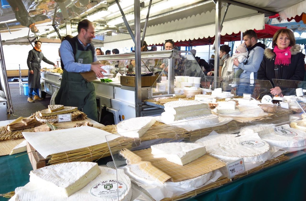 Un étal de marché présente des fromages, dont de grandes meules de brie.