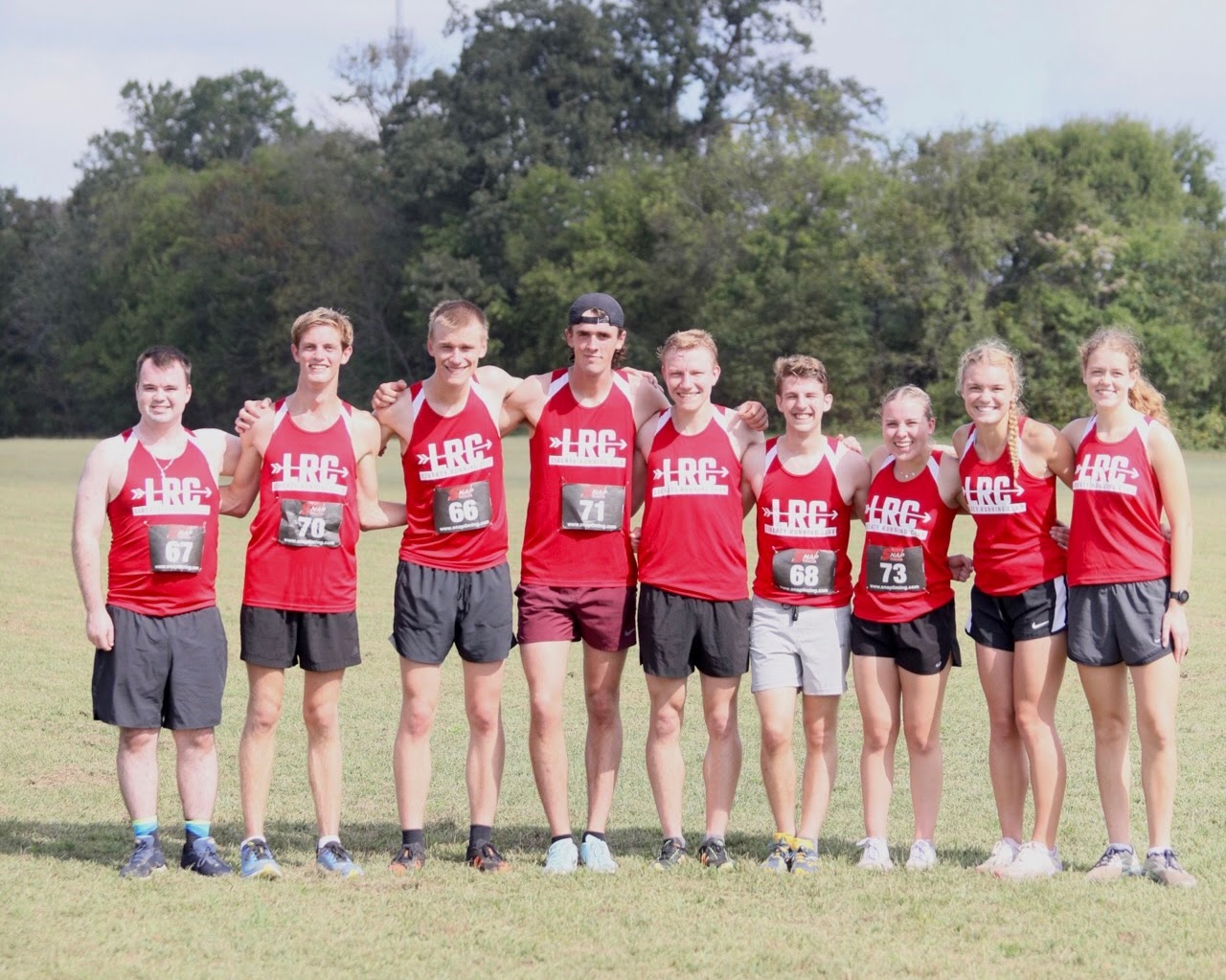 Cross country team members in red uniforms posing together on a grass field.