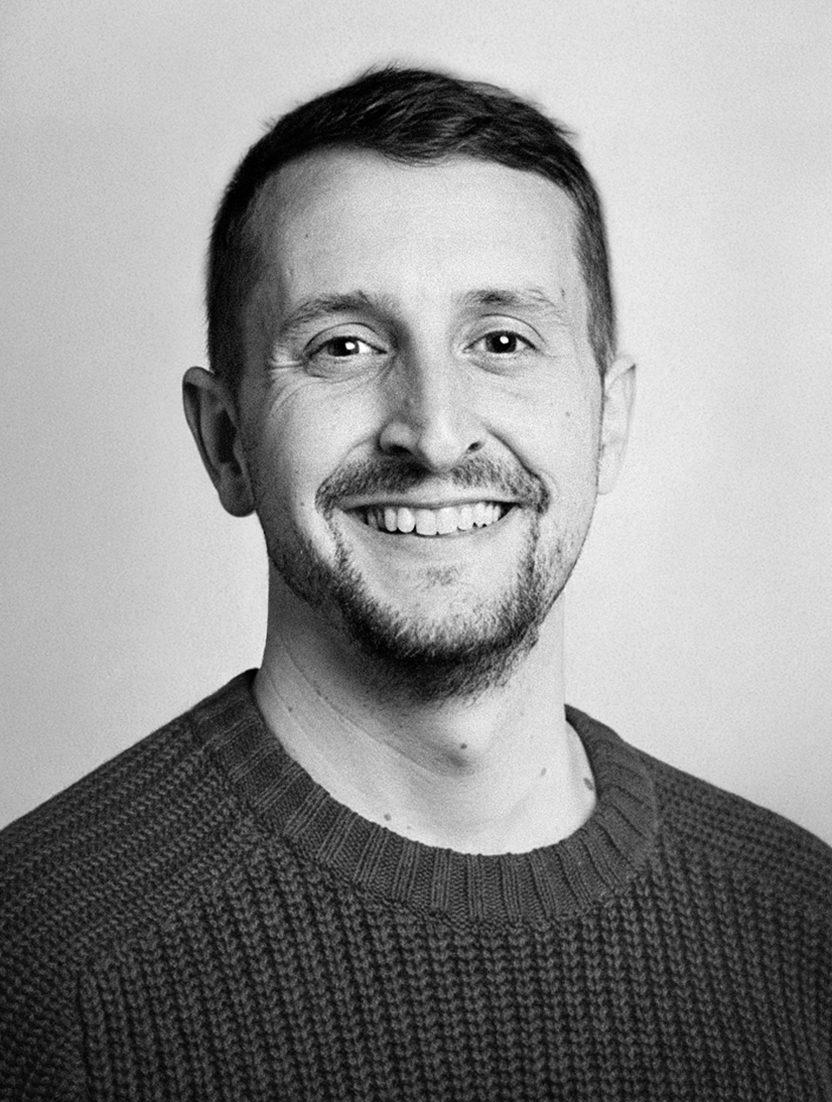 Black and white headshot of a man with short hair, a beard, and a sweater.