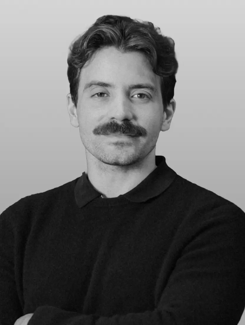 Black and white headshot of a man with dark, wavy hair, a mustache, and a dark sweater.