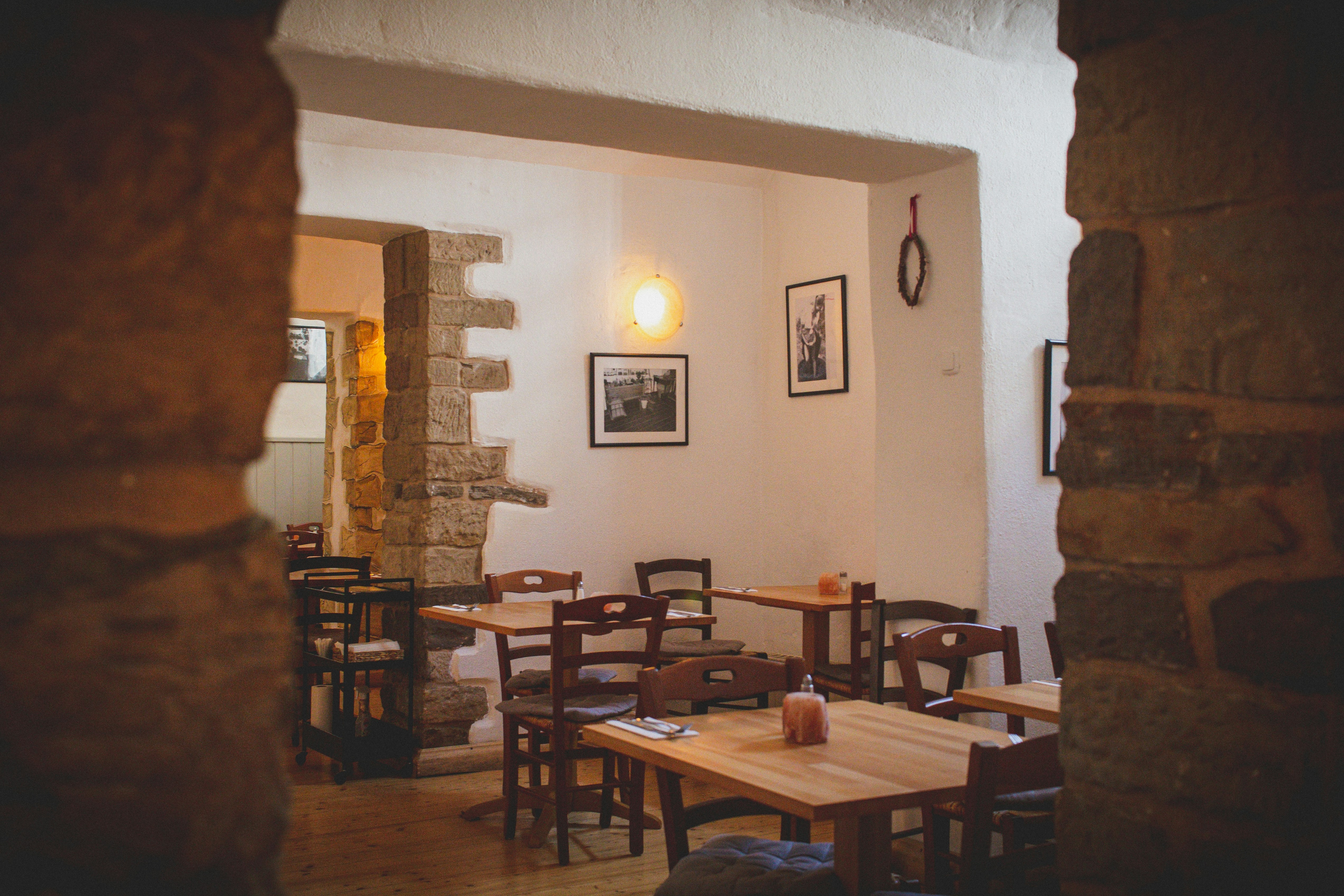 A cozy, rustic restaurant interior viewed through a stone archway, with wooden tables and chairs.